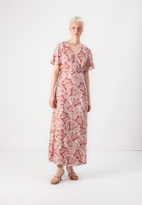 Maxi dress in coral with white floral pattern, wrap V-neck, flutter sleeves, and side slit, paired with strappy heeled sandals.