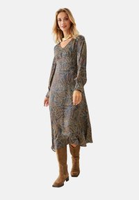 Vestido de manga larga con estampado floral en azul oscuro y escote en forma de V. Presenta una silueta fluida y se combina con botas de ante marrón hasta la rodilla.