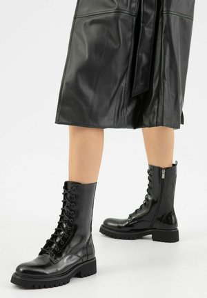 Stivali da combattimento in pelle nera presentano un'alta canna, una chiusura con lacci sul fronte e una cerniera laterale, con una suola spessa e una texture lucida.
