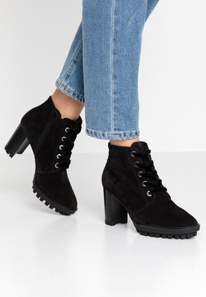 Stivaletti alla caviglia in suede nero con tacco a blocco alto, allacciatura frontale e suola in gomma testurizzata con scanalature per la trazione. Visibile denim scolorito.