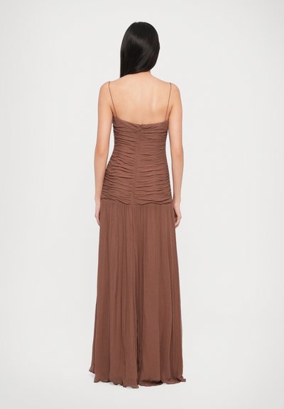 Brown maxi dress with thin straps, featuring ruched detailing at the bodice and a flowy, textured skirt. Zipper closure at the back.