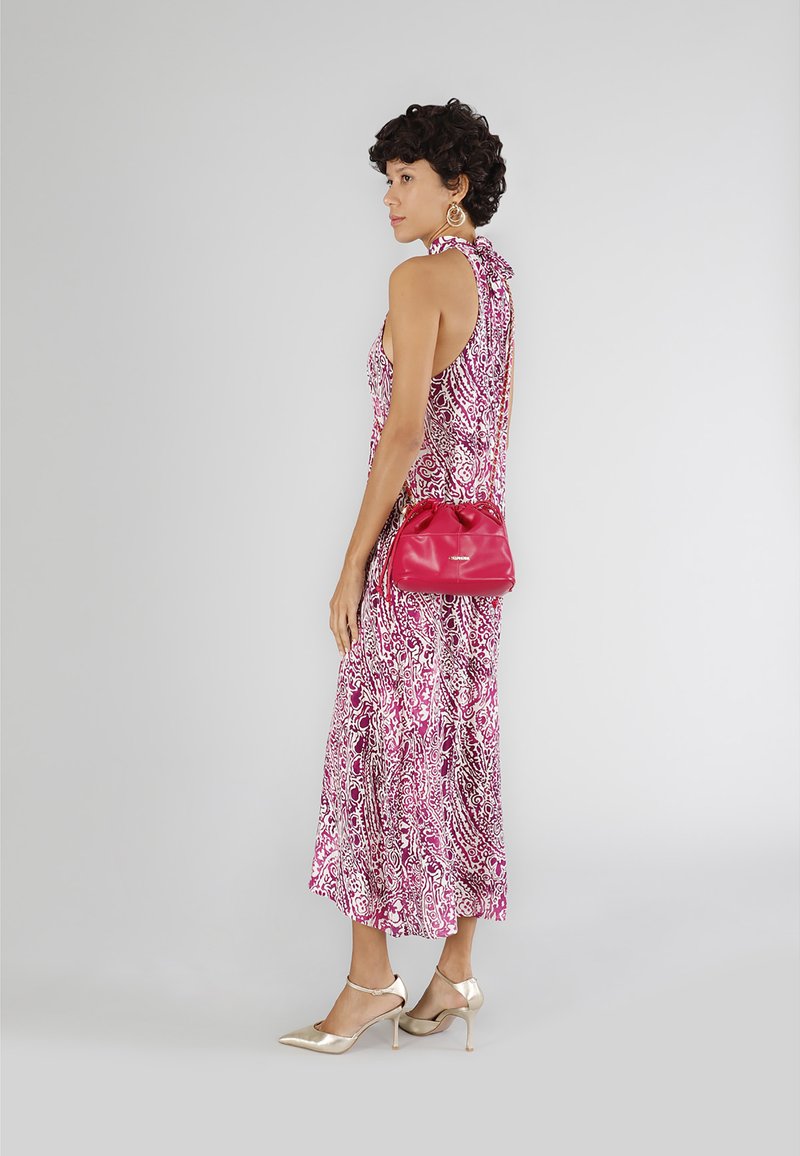 Rosa gemustertes Kleid mit Halterneck, ergänzt durch eine rote Handtasche und goldene High-Heels. Glatte Stoffstruktur sichtbar.