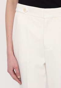 Pantaloni albi cu o croială ajustată, textură de stofă netedă, pliu frontal și un singur nasture crem la talie.