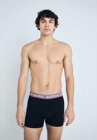 Fekete boxeralsó lilás derékkal, rajta a "BJÖRN BORG" logóval. Az anyag simának és rugalmasnak tűnik. A modell előre néz.