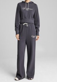 Sweat à capuche gris foncé et pantalon large assorti. Doté de cordons blancs et d'un logo brodé. Tissu doux avec une coupe décontractée.