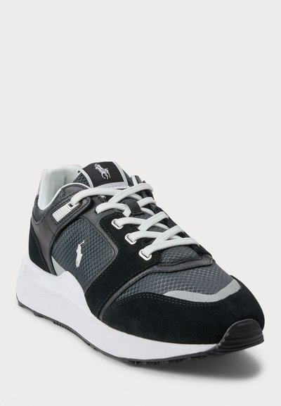 Zwarte en grijze sport sneaker met witte veters en een gevoerde witte zool, voorzien van een gestikt pony-logo aan de zijkant en op de tong.