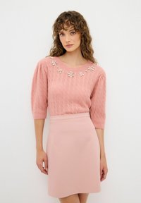 Pull en tricot rose avec des embellissements floraux autour de l'encolure, associé à une jupe moulante rose. Texture douce et finition lisse.