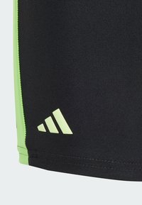 Shorts sportivi neri con una texture liscia, dotati di un pannello laterale verde neon e di un logo a tre strisce in rilievo sul bordo inferiore.