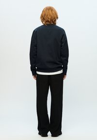 Dark navy sweatshirt with a crew neckline, ribbed cuffs, and hem, layered over a white shirt. Paired with black wide-leg pants.