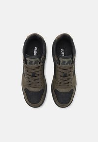 Sneakers neri e verde oliva con una tomaia testurizzata, dotati di lacci, una scatola per le dita perforata e un logo "GUESS" sulla soletta.