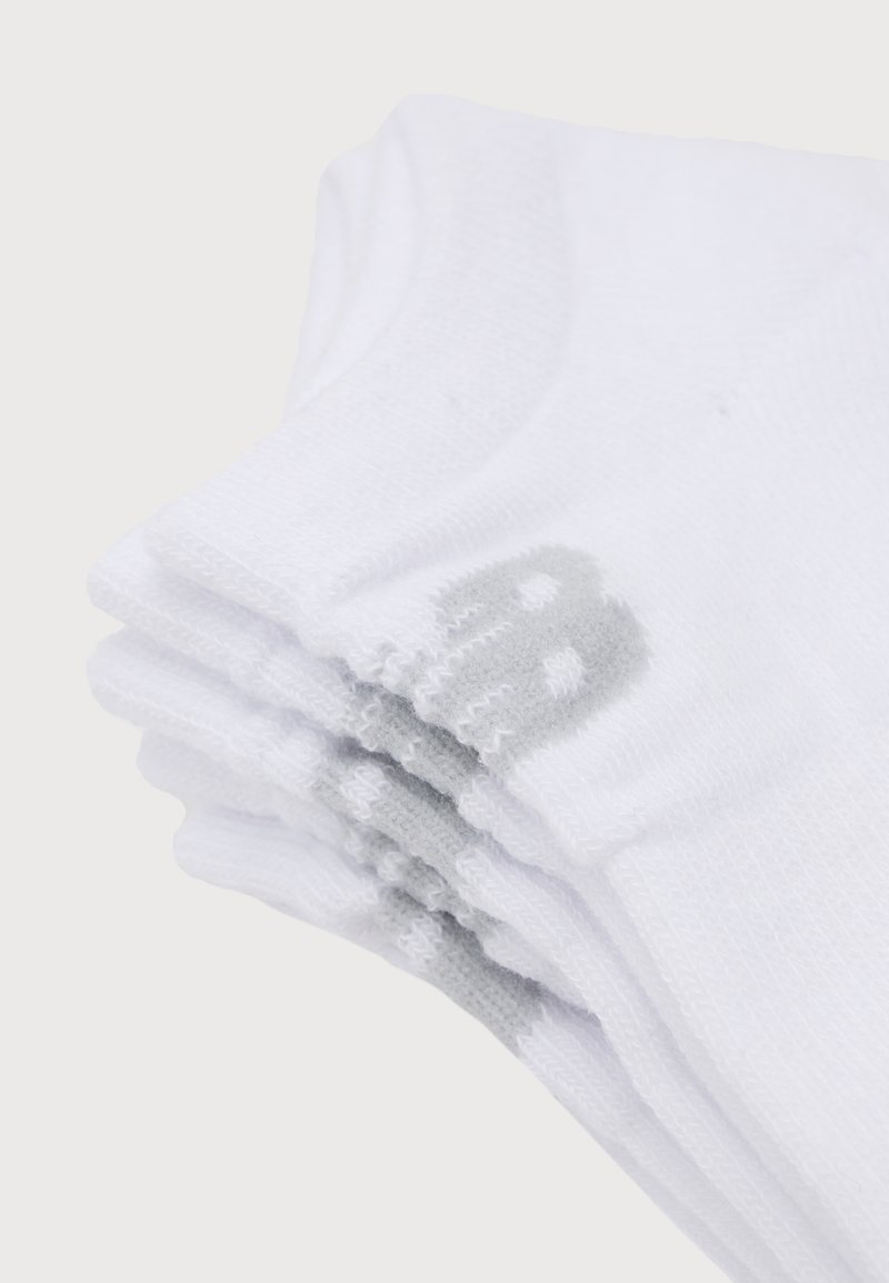 Pile de chaussettes de sport blanches à mi-mollet avec une doublure grise visible le long de la semelle et des zones de la voûte, pliées soigneusement sur un fond blanc.