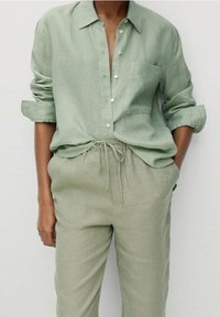 Jasnozielona lniana koszula z guzikami, z kieszenią na piersi i podwiniętymi rękawami, w komplecie z dopasowanymi, luźno dopasowanymi jasnozielonymi lnianymi spodniami.