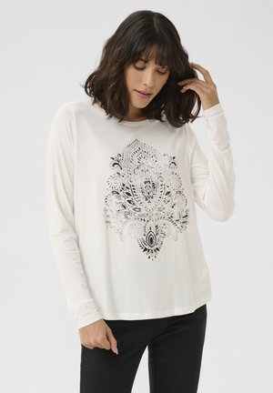 Chemise à manches longues crème avec un imprimé paisley noir intricate au centre, encolure ronde, coupe décontractée et texture douce.