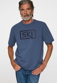 Sininen lyhythihainen t-paita, jossa on edessä suuri musta "SKI"-logo. Valmistettu pehmeästä puuvillasta, rento istuvuus. Yksinkertainen muotoilu, ei lisäkuvioita.