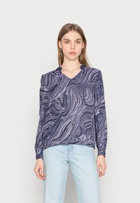 Camisola de manga longa com padrão espiral em azul marinho e branco, com decote em V e punhos franzidos, combinada com jeans azul claro.