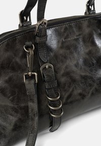 Sac à main en cuir noir avec une finition brillante, équipé de ferrures métalliques, d'une sangle réglable et d'une fermeture éclair. Les accents comprennent des anneaux circulaires.