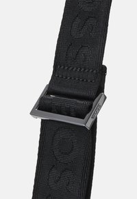 Fascia in nylon tessuto nero con logo impresso, dotata di una fibbia rettangolare in metallo nero per un attacco sicuro. Design testurizzato e resistente.