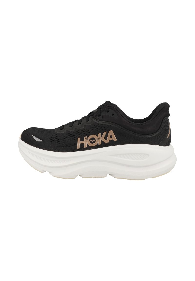 Svart løpesko med et strukturert mesh-overdel, fremtredende HOKA-logo i gull, tykk hvit mellomsåle og subtile detaljer i gummi på yttersålen.