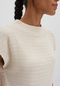 Beige short-sleeve top featuring a textured, ribbed design. Boat neck style with soft fabric in a light, neutral color.