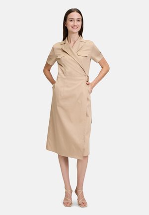 Robe enveloppante beige à manches courtes, avec poches avant et passant de ceinture. Tissu lisse, longueur au genou, présentant un design épuré et bien ajusté.