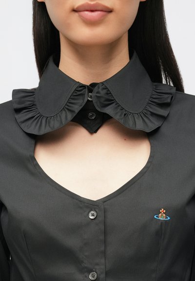 Melna krekla ar volāniem apkaklē, aizdari ar pogām un mazu izšūtu kuģa attēlu uz ūdens kreisajā pusē.