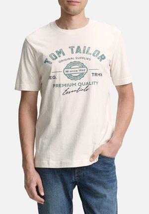 T-shirt crème avec des textes et logos verts, à manches courtes, col rond, fabriqué en coton doux, coupe décontractée.
