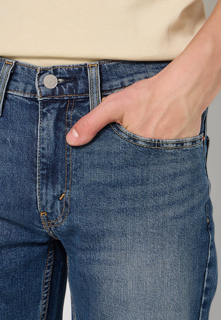 Blå denimjeans med standard passform, som har en framficka, kontrasterande sömmar och en metallknapp i midjan.