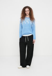 Ανοιχτό μπλε πουλόβερ με σχέδιο λεοπάρ σε μπεζ, συνδυασμένο με φαρδιά μαύρα παντελόνια και λευκά αθλητικά παπούτσια. Πλεκτό υλικό με υφή.