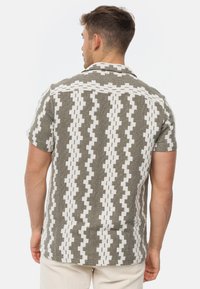 Chemise à manches courtes en vert olive et blanc avec un motif géométrique, arborant un tissu texturé et un col.