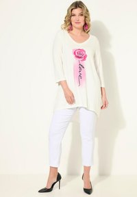 Tunica bianca con grafica di una rosa rosa e testo "love", abbinata a pantaloni bianchi. Presenta un collo a giro e maniche a tre quarti.