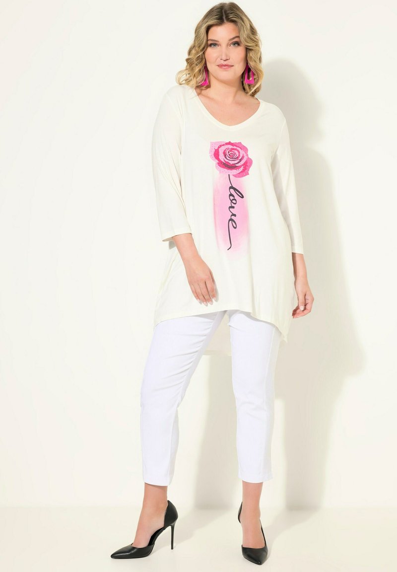 Tunica bianca con grafica di una rosa rosa e testo "love", abbinata a pantaloni bianchi. Presenta un collo a giro e maniche a tre quarti.