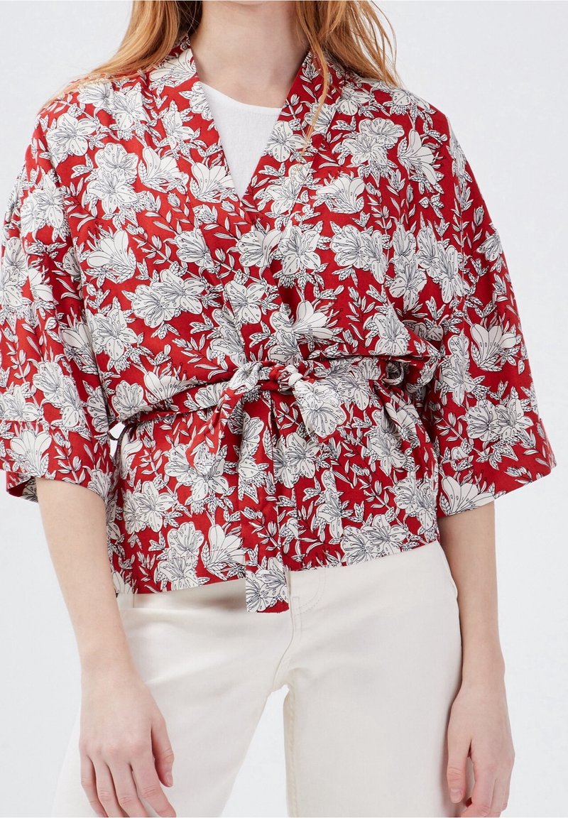 Red floral kimono-style top with short sleeves, featuring white floral patterns, and a tied waist detail. Lightweight fabric, relaxed fit.