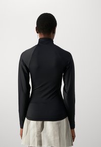 Långärmad svart topp med hög krage, slät yta, figurnära design och en söm på baksidan. Bärs med en lätt, texturerad kjol.