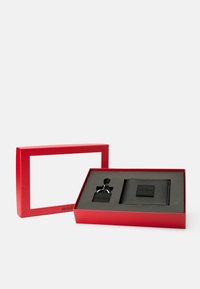 Conjunto de carteira de couro preto e chaveiro em uma caixa de presente vermelha com uma janela transparente. A carteira apresenta um logótipo em relevo; o chaveiro tem um acabamento metálico.