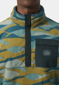 Sudadera de forro polar con patrones abstractos en azul, amarillo y verde; cuello alto; bolsillo frontal negro con logotipo; botones a presión y textura suave.