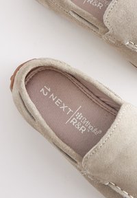 Chaussure à enfiler en daim beige clair avec semelle intérieure en tissu marron portant l'étiquette "NEXT 42" et bord visible de semelle en caoutchouc marron.