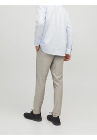 Světle modrá košile s dlouhým rukávem a světle šedé kalhoty na míru, v kombinaci s černými botami; viditelné švy a detaily skládání na kalhotách.