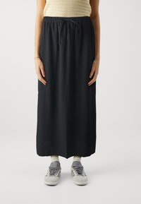 Svart, lang skjørt laget av et lett materiale, med elastisk midje og snor. Kombinert med grå joggesko og hvite sokker.