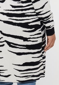Black and white zebra-striped cardigan with a soft texture, ribbed hem, and a slightly tapered shape. Close-up of the back detail.