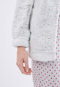 Jasnoszara, puszysta kurtka z futerka sztucznego z podwiniętym mankietem, w połączeniu z szarymi spodenkami piżamowymi ozdobionymi małymi czerwonymi wzorami serc.