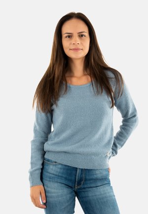 Maglione azzurro chiaro con una texture morbida, scollatura rotonda e polsini a costine, abbinato a jeans blu. Piccolo dettaglio decorativo all'orlo.