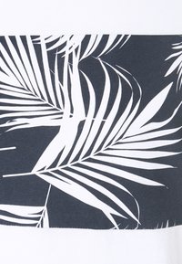 Kurzarmhemd mit einem weißen und dunkelgrauen Design, auf dem ein horizontaler Streifen mit weißen Palmenblättern zu sehen ist. Texturierte Stoffdetails am Saum.