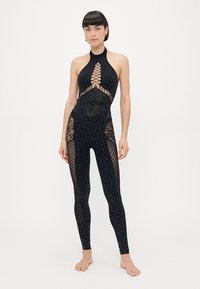 Black bodysuit with a high neckline and open weave accents, adorned with a pattern of small white dots. Textured mesh side panels.