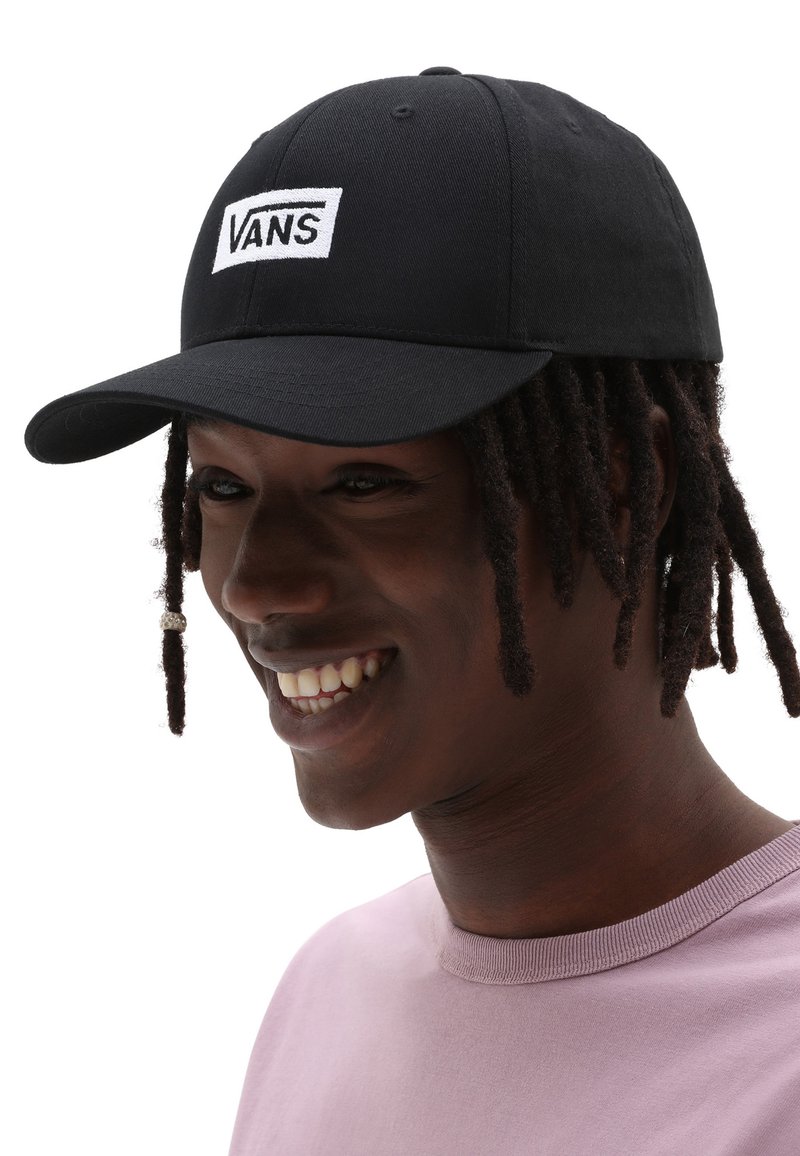Gorra de béisbol negra de tela, con un logo bordado en blanco que dice "VANS". La gorra tiene un visor curvado y un diseño ajustado.