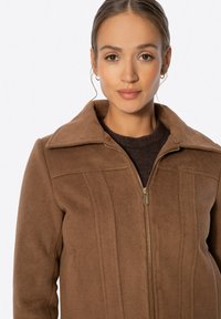 Braune Fleecejacke mit Reißverschluss vorne, weitem Kragen und vertikalen Nahtdetails. Strukturierter Stoff mit einer weichen Haptik und subtiler Strahlung.