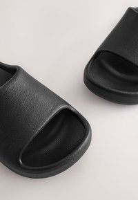 Schwarze Sandalen mit offenem Zehenbereich aus strukturiertem synthetischem Material, mit geschwungenem Design und flachen Sohlen. Glatte Innenseite für Komfort.
