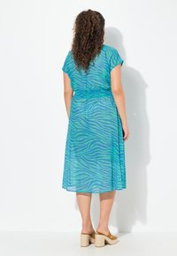 Maxime dress in sheer turquoise fabric with a blue zebra pattern. Features short sleeves and a cinched waist design.