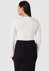 Vit långärmad topp med rundad halsringning, ihop med en svart penningkjol med dragkedja bak och en figurnära silhuett.