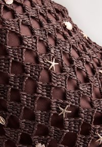 Dark brown woven net fabric with small gold starfish and seashell charms attached in a scattered pattern.