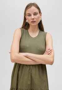 Bezramenné olivově zelené šaty s přiléhavým topem a rozšířenou sukní. Lesklé akcenty na živůtku, hladká bavlněná tkanina a vrstvený design.
